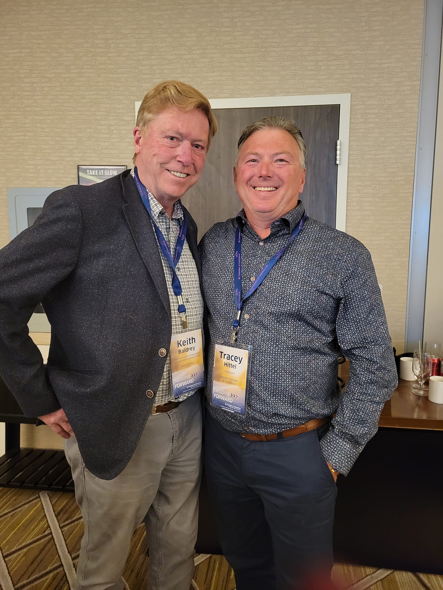 Two men dressed for business and wearing conference badges smile for a photo opportunity.