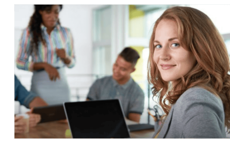Confident businesswoman smiling at the camera while colleagues collaborate in the background, symbolizing professional networking and leadership.