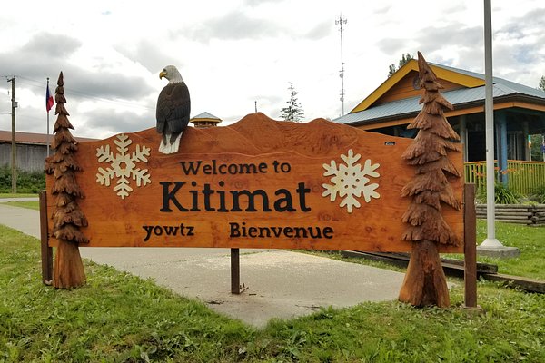 Carved wooden welcome sign at the Kitimat Chamber of Commerce featuring snowflakes, trees, and a perched eagle, with the text 'Welcome to Kitimat – yowtz – Bienvenue' in English, Haisla, and French