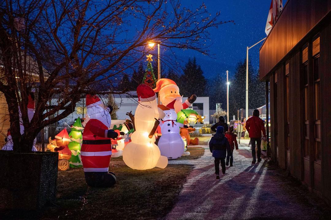 Families walking through a holiday light display at night in Kitimat, surrounded by glowing inflatable Santas, snowmen, and Christmas trees during the Light Up Kitimat event.