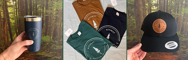 Kitimat Chamber’s Coastline Collective merchandise display featuring a stainless steel travel mug, branded t-shirts, and hats with the Kitimat logo, locally made gifts and souvenirs from the Chamber Gift Store.